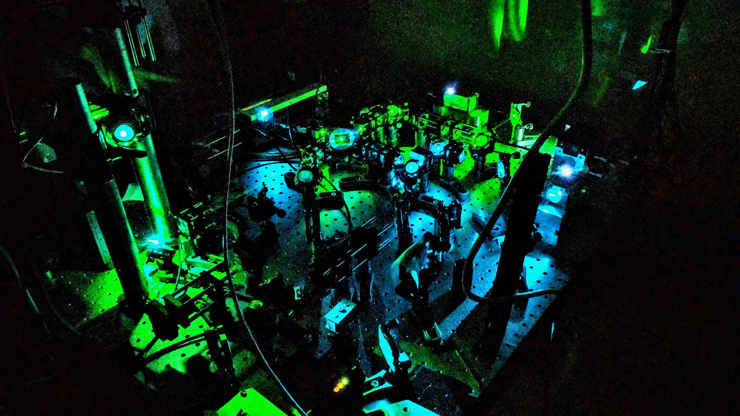 Cage-mounted optics on an optical table lit by green and blue laser light